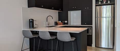 A modern kitchen with a central island, black cabinets, stainless steel appliances, and bar stools.