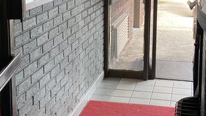 A hallway with a red carpet leading to a door, brick walls, and a window with a view of the street. - Deer Park Motor Inn (Deer Park)
