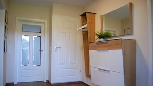 Un couloir avec une porte blanche, un plancher en bois, un meuble blanc avec un miroir et une petite plante posée sur le dessus.