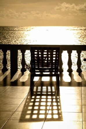 Un banc à motifs géométriques, placé sur un sol carrelé, donnant sur une étendue d’eau avec une rambarde au premier plan.