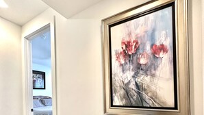 Un pasillo con un cuadro enmarcado de flores en la pared, piso de madera y una puerta que da a un dormitorio.