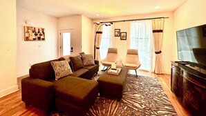 Una sala de estar con un sofá, dos sillones, una mesa de centro, un televisor y un tapete estampado.
