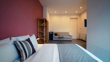 Una habitación de hotel moderna con cama, armario, sofá y una mesita.
