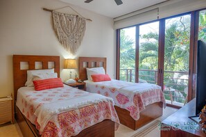 A hotel room with two beds, a large window with a view of greenery, a ceiling fan, and a macrame wall hanging. - Spacious beachfront condo  with AC, WiFi, swimming pool! (AKUMAL)