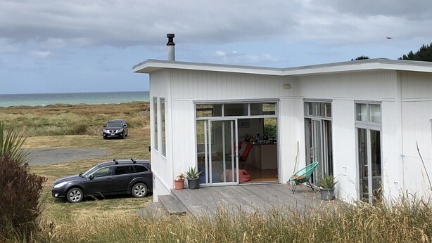 A modern house with a deck, large windows, and a view of the ocean. - Wairarapa Bach Flat Point (Flat Point)