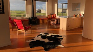 A spacious living room with a large window, a fireplace, and a cowhide rug. - Wairarapa Bach Flat Point (Flat Point)