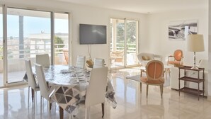 A spacious living area with a large dining table, comfortable seating, a flat-screen TV, and a balcony with a view. - 3-Br. Apartment, Sea View, Swimming Pool. (Cannes)