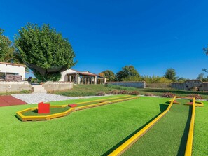 Un barrio residencial con un césped cuidado, un parque infantil rojo y una casa con techo de tejas y paredes de piedra.