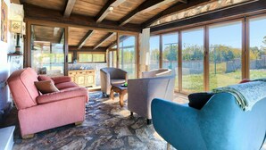 A spacious room with a stone floor, wooden ceiling beams, and large windows offering a view of the outdoors. - Wonderful private villa for 8 guests with A/C, private pool, WIFI, TV, patio and pets allowed (Muntic)