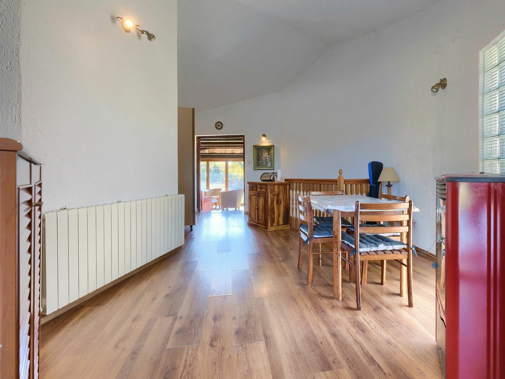 Ein geräumiger Raum mit Holzboden, einem Esstisch mit Stühlen, einem Heizkörper und einem roten Schrank.