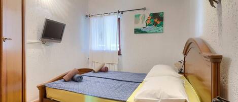 A bedroom with a bed, a television, a window with curtains, and a painting on the wall.