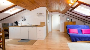 A cozy attic bedroom with a kitchenette, wooden beams, and a blue sofa with pink pillows.