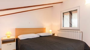 A bedroom with a bed, two bedside lamps, a window with blinds, and a radiator.