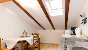 A compact kitchen with a dining area, wooden beams, a skylight, and basic amenities.