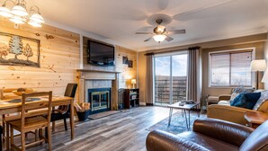 Ein gemütliches Wohnzimmer mit Kamin, Holzwänden, Deckenventilator und großem Fenster.