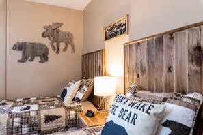 Une chambre à coucher avec une courtepointe à carreaux, une lampe et des œuvres d’art murales, dont une représentation d’un élan et un panneau indiquant le mot « AVENTURE ».