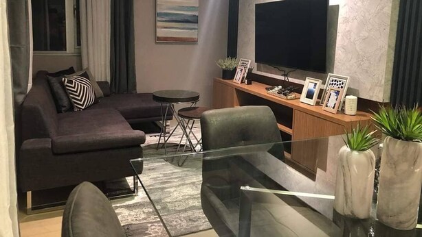 A modern living room with a sofa, a glass coffee table, and a TV mounted on the wall.