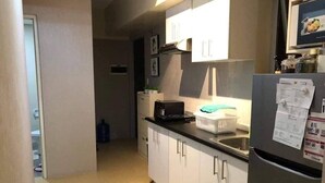 A compact kitchen with white cabinets, a black countertop, and a refrigerator with papers on it.