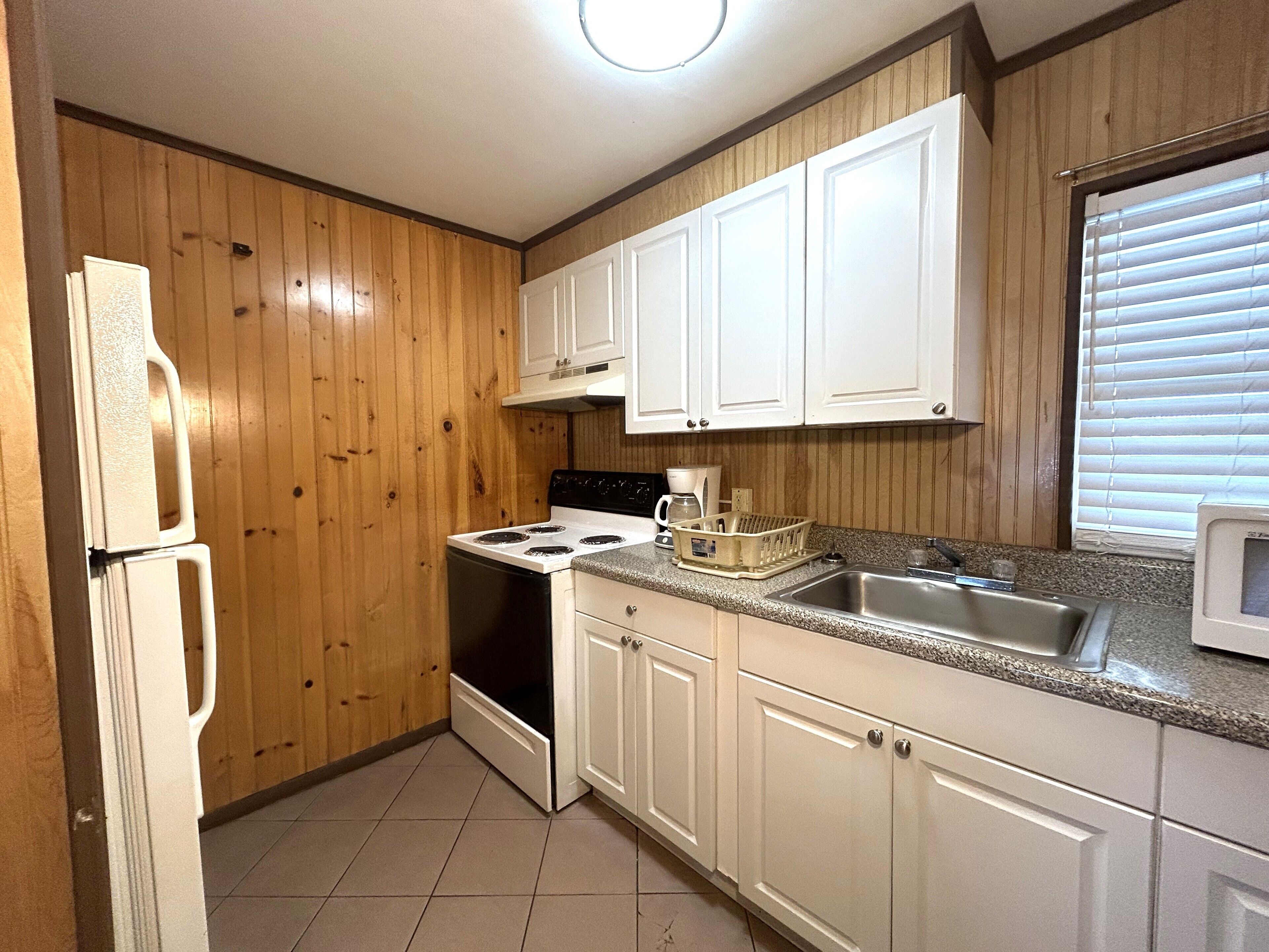 A kitchen with wooden paneling, white cabinets, a stove, a refrigerator, and a microwave.