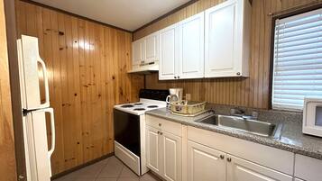 Una cocina con paneles de madera, armarios blancos, una estufa, un refrigerador y un microondas.