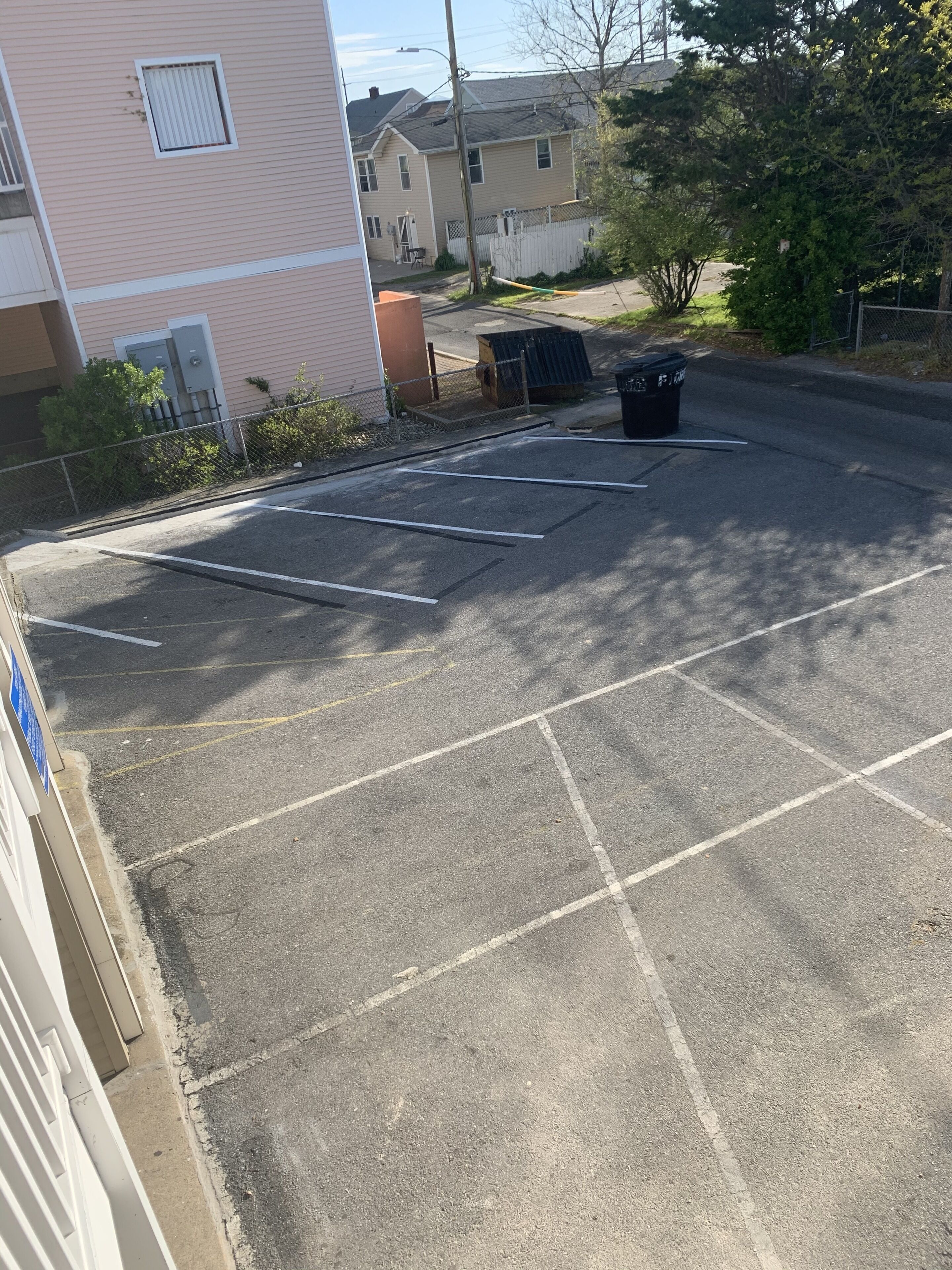 Un parking avec des places délimitées, une poubelle et un bâtiment en arrière-plan.
