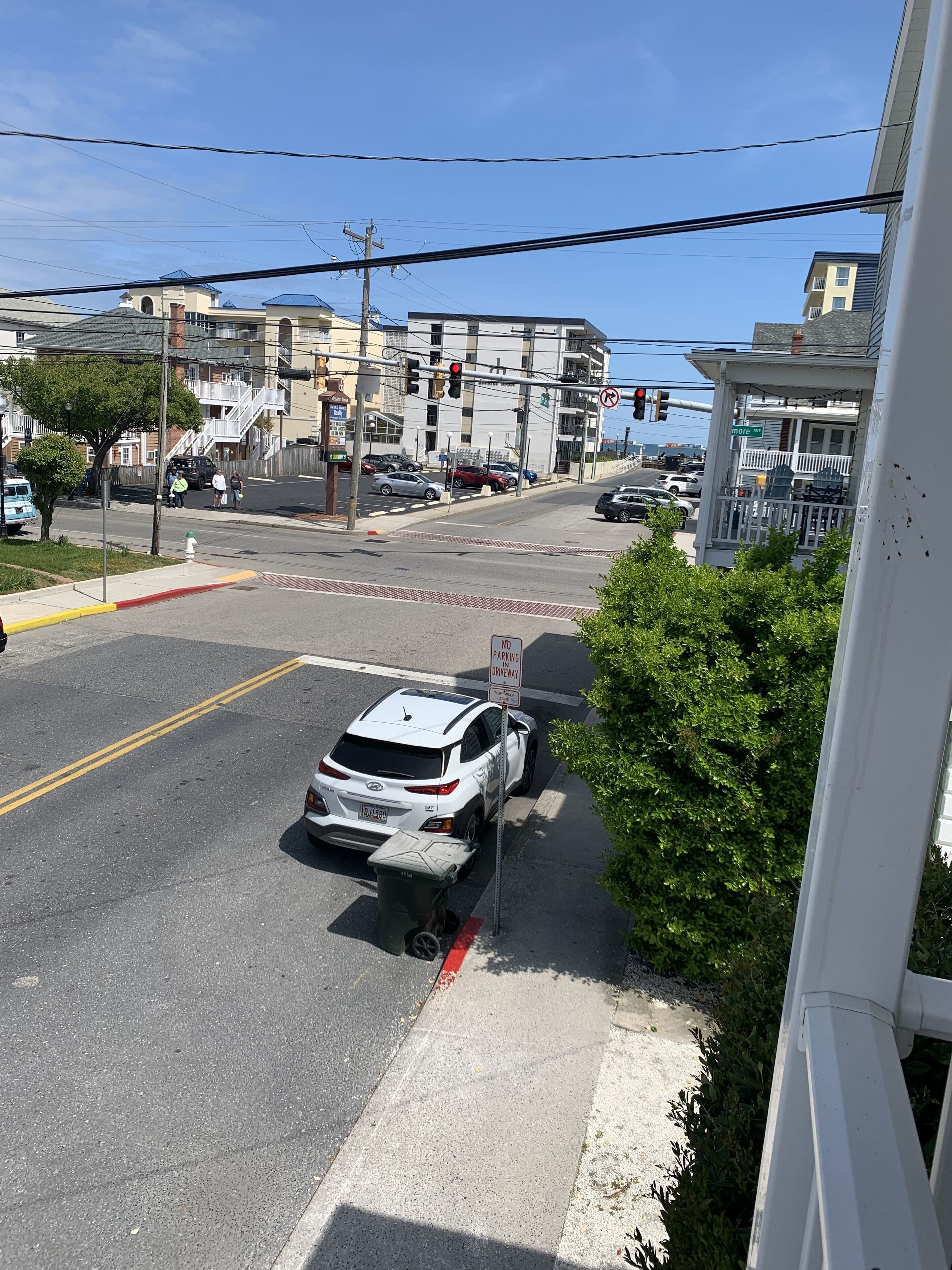 A street view with a white SUV parked on the side, a 'No Parking' sign, and a 'No Parking Driveway' sign.