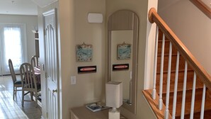 A hallway with a wooden staircase, a light fixture, a table with a lamp, and a door leading to a dining area. - Wilmington Terrace (Ocean City)