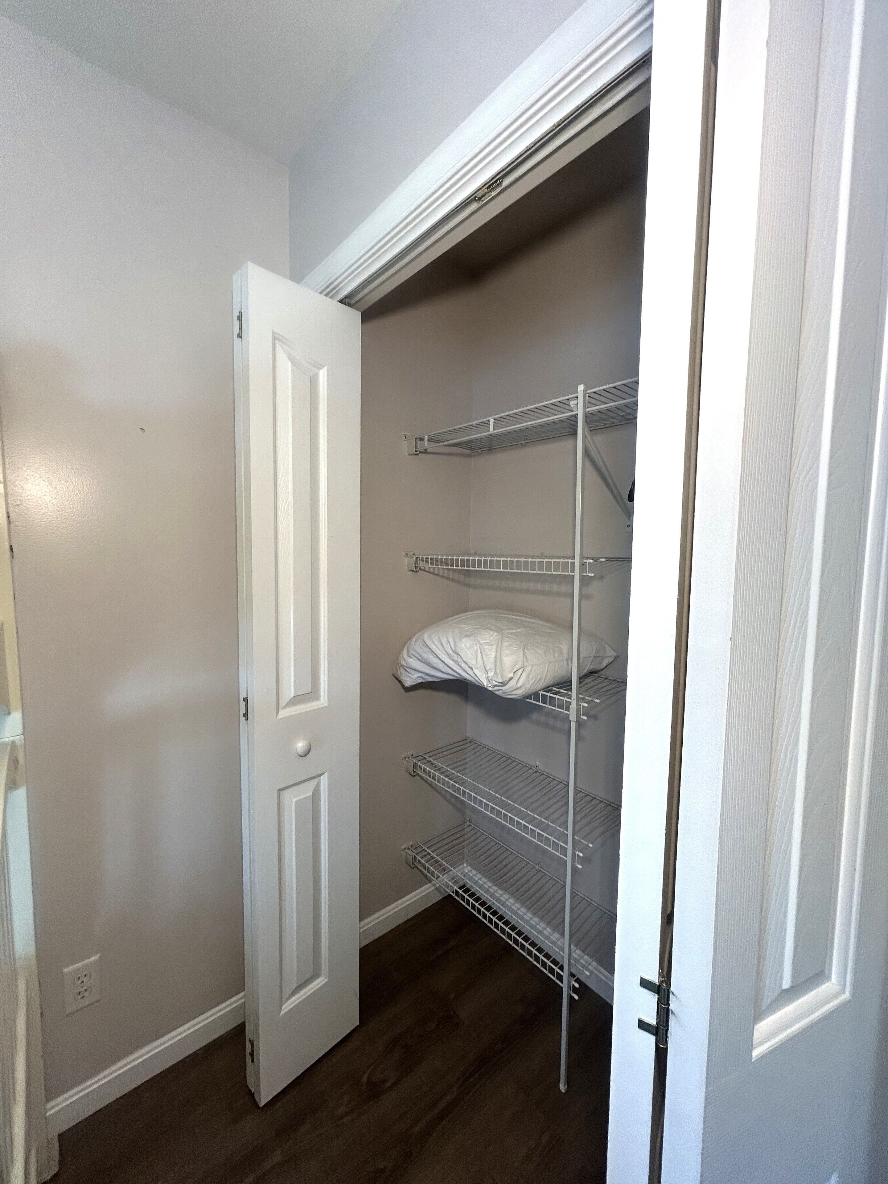A walk-in closet with a white door, metal shelving, and a dark wood floor.