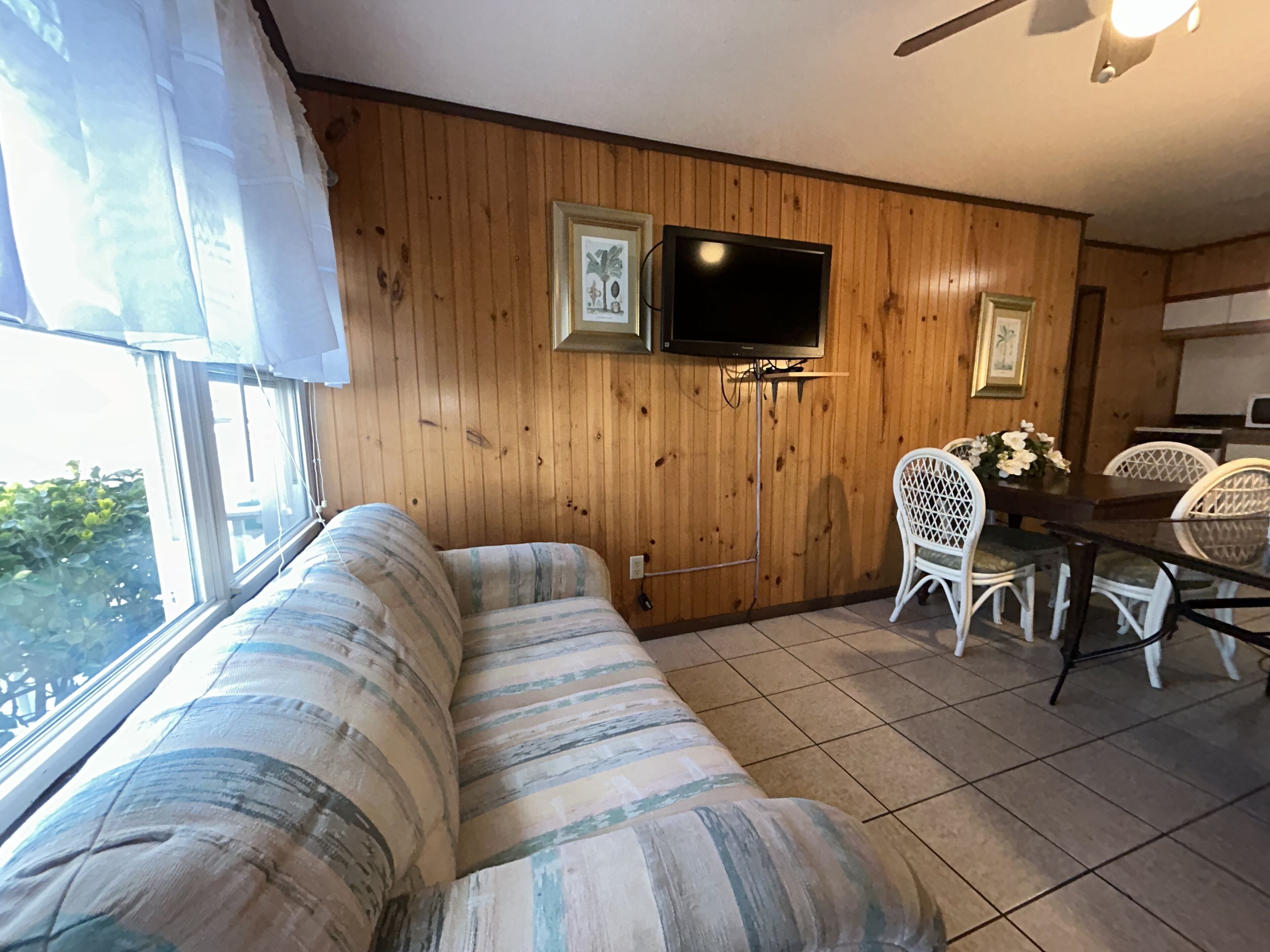 Una habitación acogedora con una pared de madera, un sofá, una mesa de comedor con sillas y un televisor colgado en la pared.