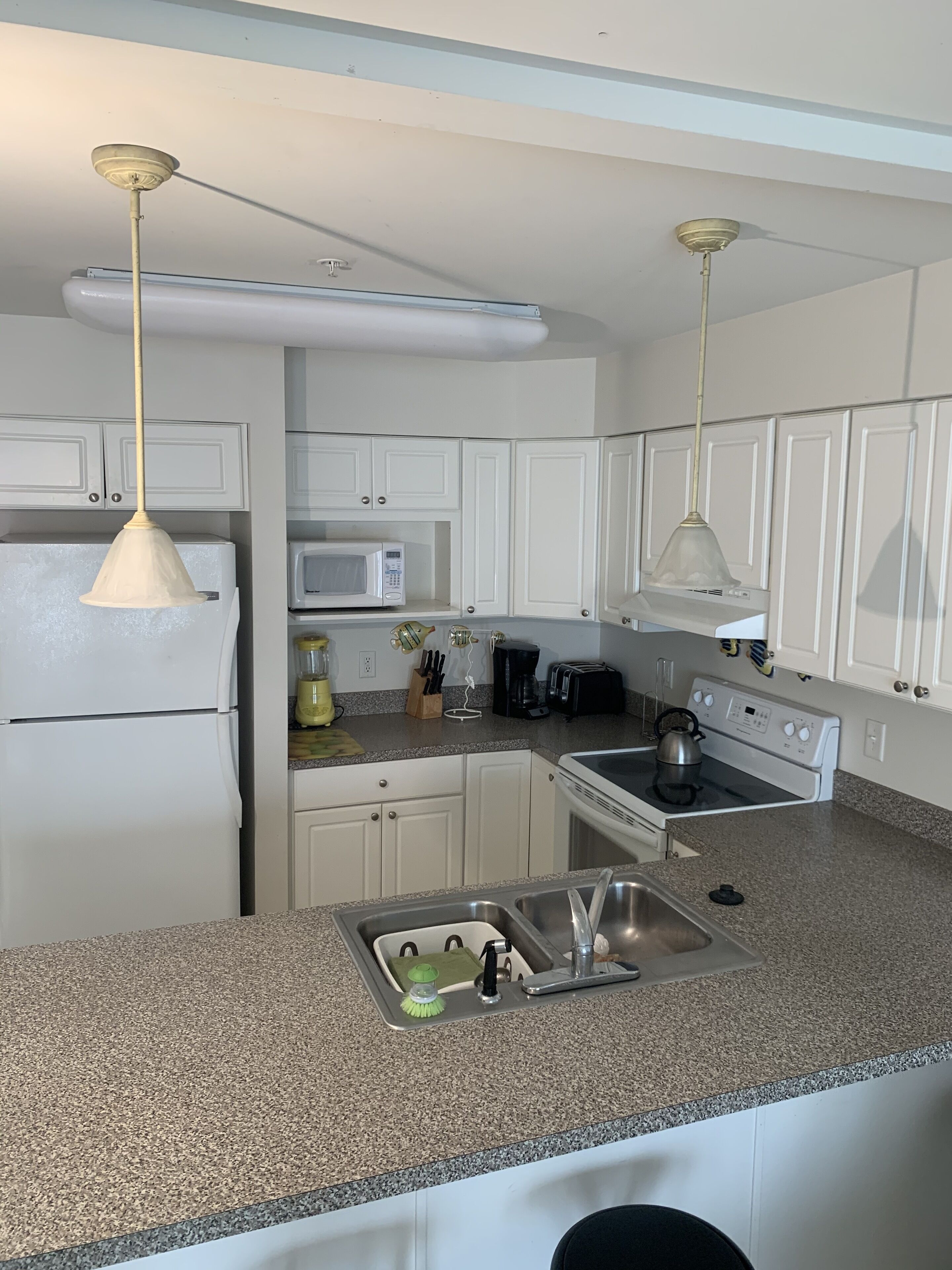 A kitchen with white cabinets, a stainless steel sink, a microwave, a stove, and two pendant lights.