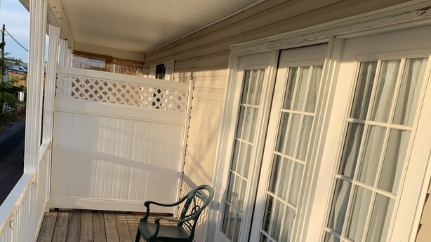 A covered porch with wooden flooring, white railings, and two green chairs. - Wilmington Terrace (Ocean City)