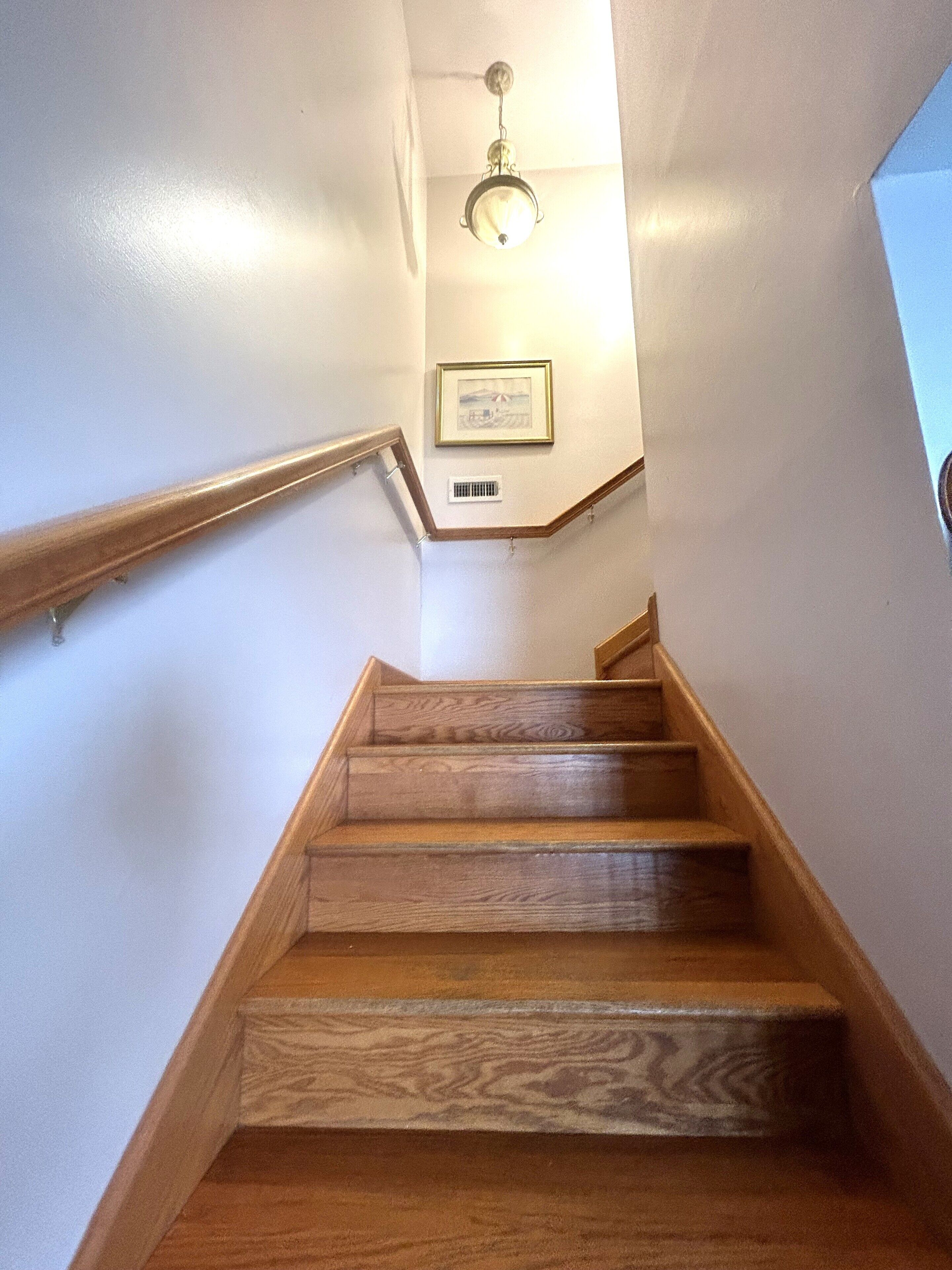 A wooden staircase with a handrail, a light fixture, and a framed picture on the wall.