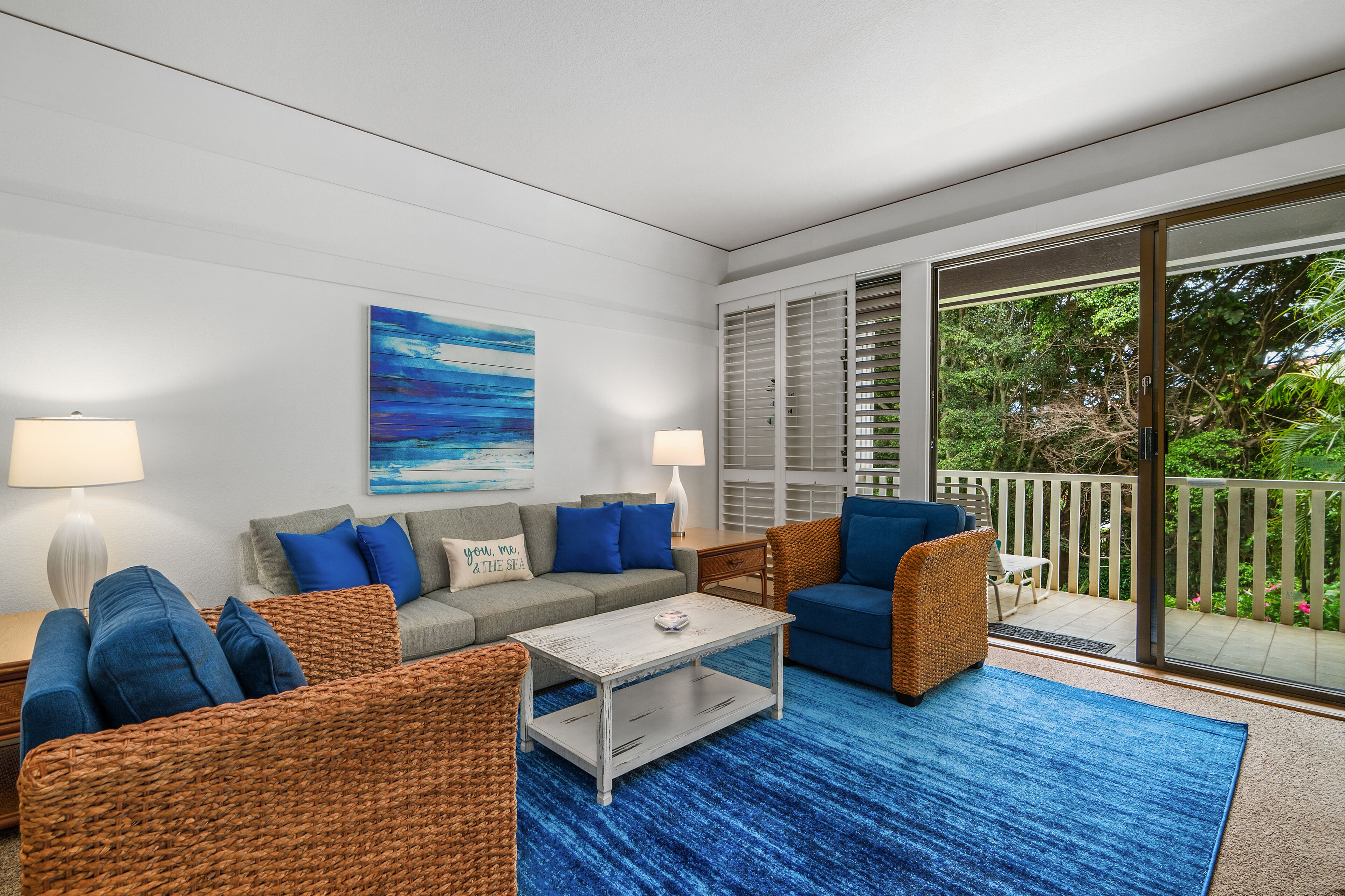 A modern living room with a grey sofa, blue cushions, wicker furniture, and a blue rug.
