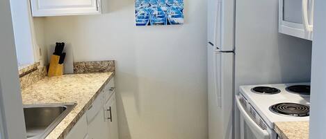 A compact kitchen with white cabinets, a granite countertop, a sink, a refrigerator, a microwave, and a stove.