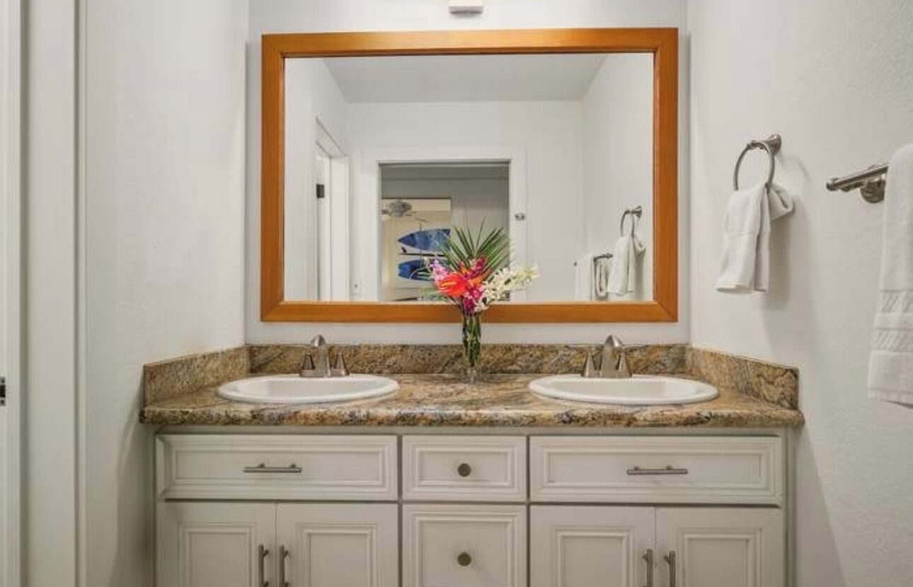 Un baño con dos lavamanos, un espejo grande y un florero con flores.