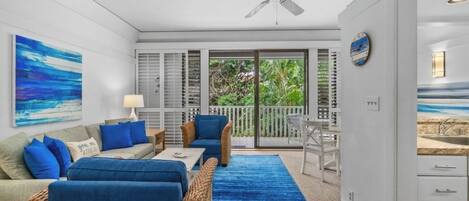 A modern living room with a blue carpet, a ceiling fan, and a view of the outdoors through a sliding glass door.
