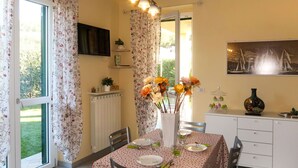 A dining area with a table set for two, a radiator, a TV mounted on the wall, and a painting above the table. - Lovely apartment for 4 people with WIFI, A/C, TV, patio and pets allowed (San Bartolomeo Al Mare)