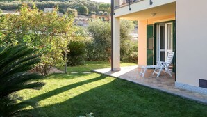 A two-story building with a balcony, a patio with two white chairs, and a well-maintained garden. - Lovely apartment for 4 people with WIFI, A/C, TV, patio and pets allowed (San Bartolomeo Al Mare)