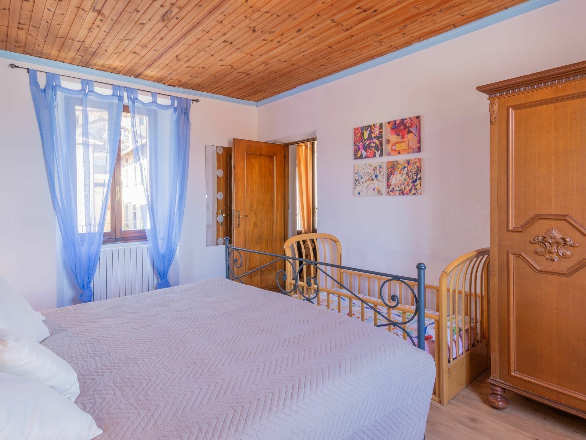 A bedroom with a bed, a wooden wardrobe, a chair, and a door with a mirror.