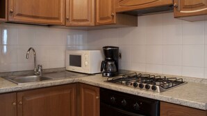 Una cocina con armarios de madera, un lavamanos de acero inoxidable, un microondas, una cafetera y una estufa a gas.