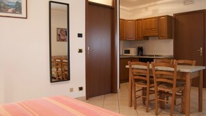 Una habitación con una cama, una mesa de comedor con sillas, armarios de madera, un microondas y una cafetera.