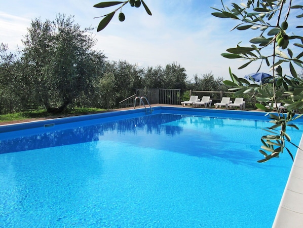 A clear blue swimming pool with a metal ladder, surrounded by white lounge chairs and a metal fence.