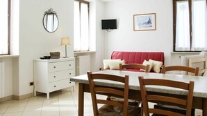 A dining area with a table, chairs, a white cabinet, a mirror, a television, and a window with curtains. - Lovely apartment in villa for 4 guests with A/C, WIFI, pool, TV and panoramic view (Bardolino)