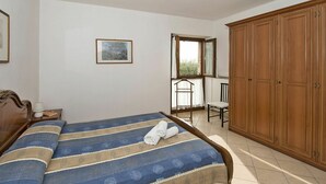A bedroom with a bed, a wooden wardrobe, a chair, a window, and a framed picture on the wall. - Lovely apartment in villa for 4 guests with A/C, WIFI, pool, TV and panoramic view (Bardolino)