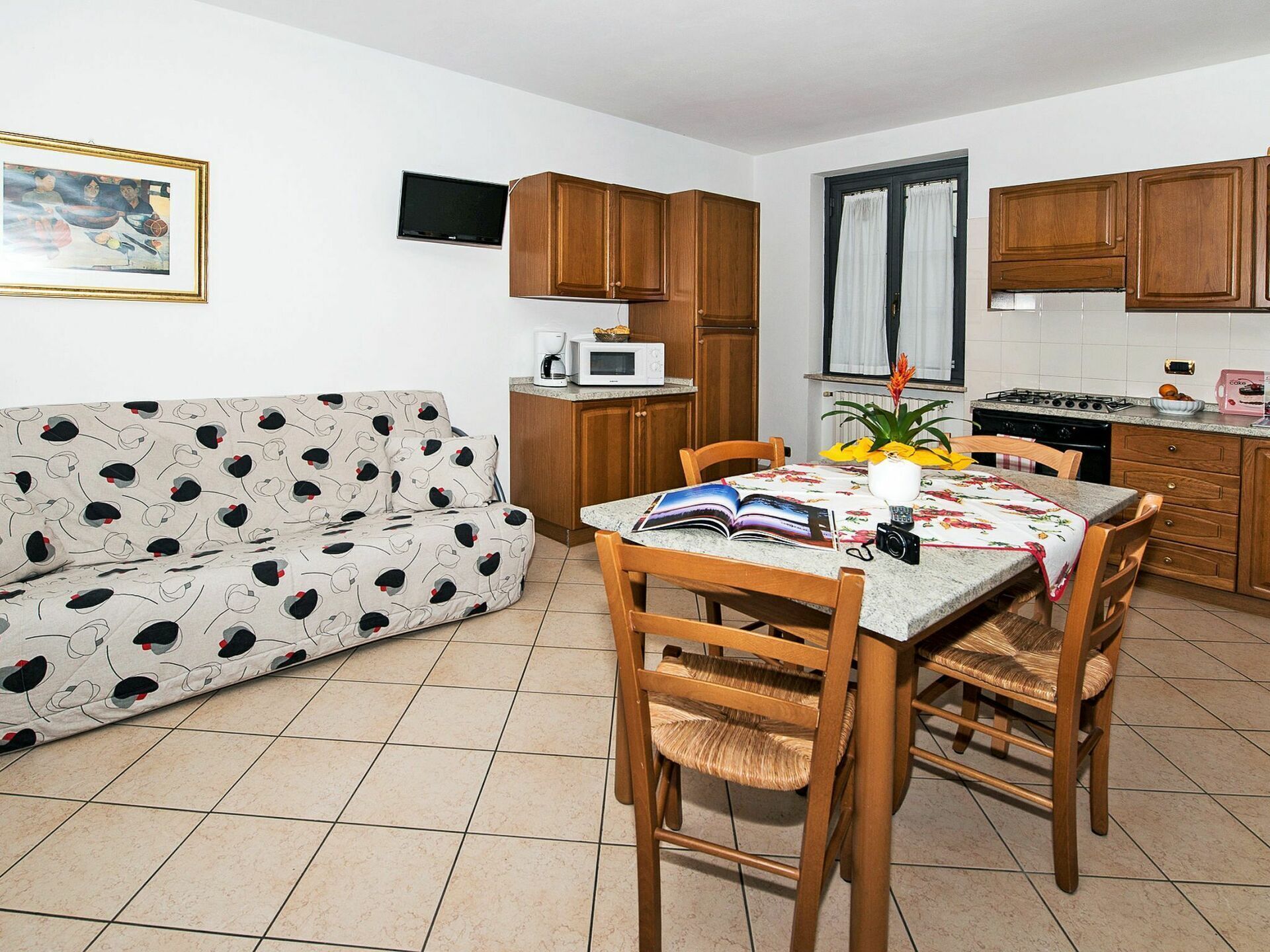 A compact living space with a sofa, dining table, chairs, a kitchen area with cabinets, a microwave, and a window with curtains.