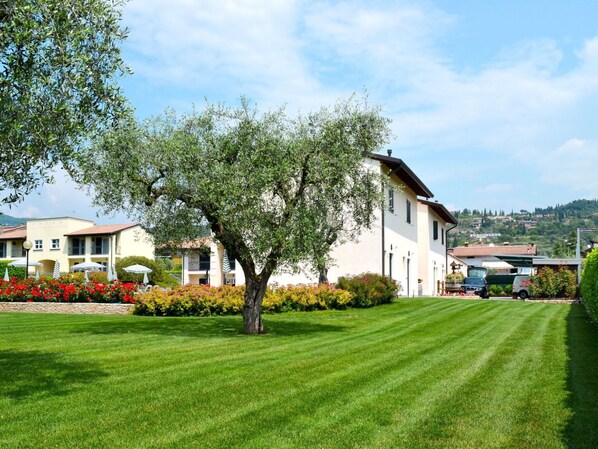 A well-maintained lawn with a large tree in the center, surrounded by neatly trimmed hedges and colorful flower beds.