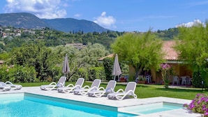 Una piscina con sillas de descanso, vista a un paisaje montañoso y un edificio con techo de tejas.