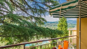 Ein Balkon mit einem Tisch für zwei Personen, einer Obstschale, einer Kanne und einem orangefarbenen Getränk.