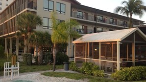 A modern hotel with a covered outdoor seating area, a pool, and a well-maintained garden. - Fabulous DIRECT Oceanfront, private beach, shelling & steps to beach, no traffic (Fort Myers Beach)