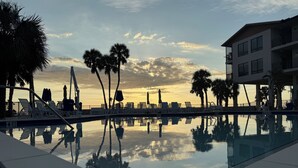 A poolside area with lounge chairs and umbrellas, palm trees, and a building with balconies. - Fabulous DIRECT Oceanfront, private beach, shelling & steps to beach, no traffic (Fort Myers Beach)